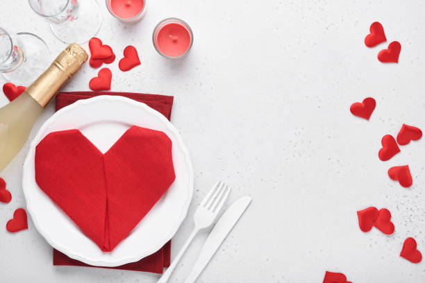 istock Valentinas day table setting white color with white silverware, red napkin folded as heart, candles, champagne, glasses on white background for greetings. Romantic dinner or menu concept. Mock up. 1360495537
