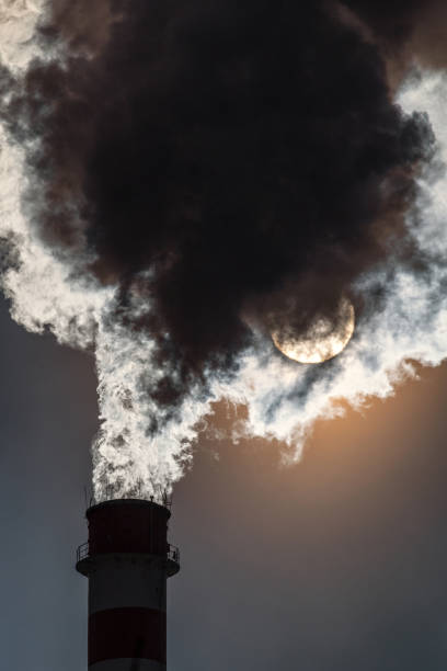 istock factory chimney and coming out dark smokes in the sky and sun at background 1360495708