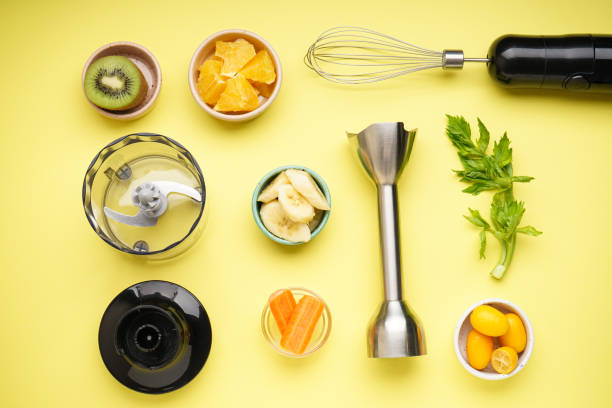 istock Hand blender and accessories with sliced fruit on a yellow background. Top view. 1360498955