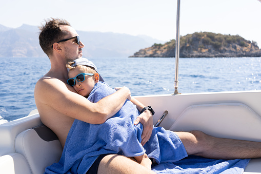 The child sleeps in his father's arms on board a water vessel. International Father's Day.