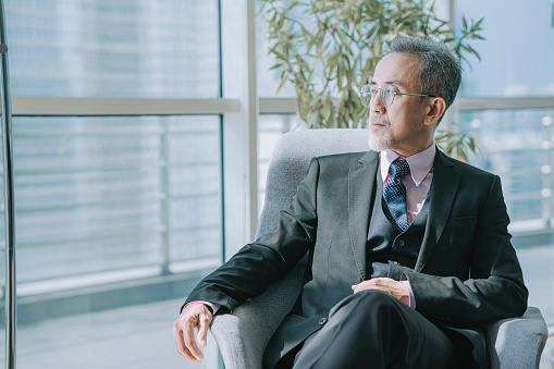 Successful Asian Chinese Senior Manager looking away sitting at office lounge