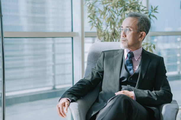 successful asian chinese senior manager looking away sitting at office lounge - 僅老年男人 個照片及圖片檔