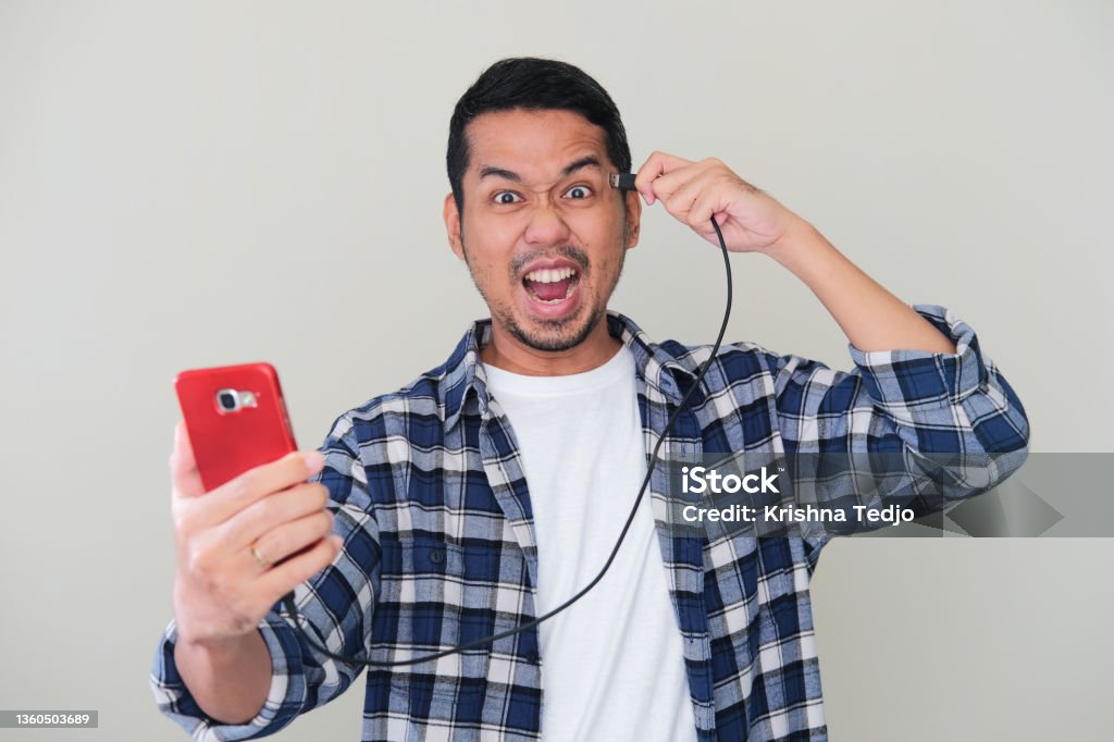 Adult Asian man screaming crazy while plug in a cabel data from mobile phone to his head Head Stock Photo