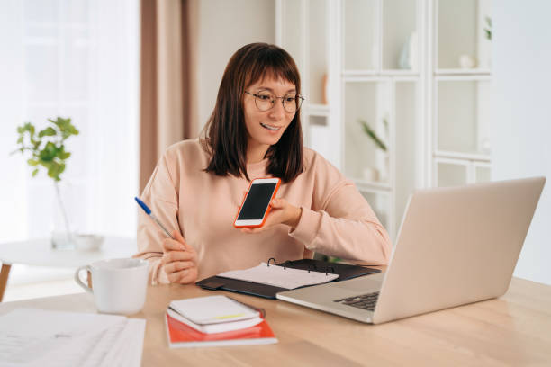 istock Pretty female recording voice message on smartphone while working remotely 1360503779