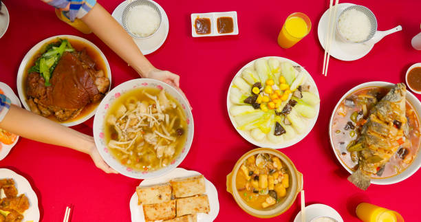 chinese new year concept - high angle view of family members serving many traditional foods on red dining table together