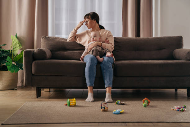 Young tired woman suffering from postnatal depression at home Tired single mother suffering from postpartum depression. Exhausted frustrated woman holding her toddler baby on knees, feeling stressed with sleepless nights and stressful motherhood difficulties worried mom with kids stock pictures, royalty-free photos & images