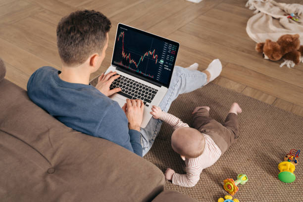 Young business dad making money as crypto trader investor broker while babysitting at home Businessman, crypto trader investor and young father working from home, using laptop with stock market app for cryptocurrency financial stock market analysis while his toddler baby playing nearby stock brokers stock pictures, royalty-free photos & images