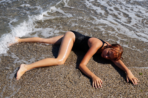 teen girl sunbathes on wet sand near the water on the beach.