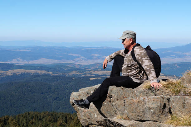 istock a man sits on a mountain top with a backpack and contemplates 1360506118