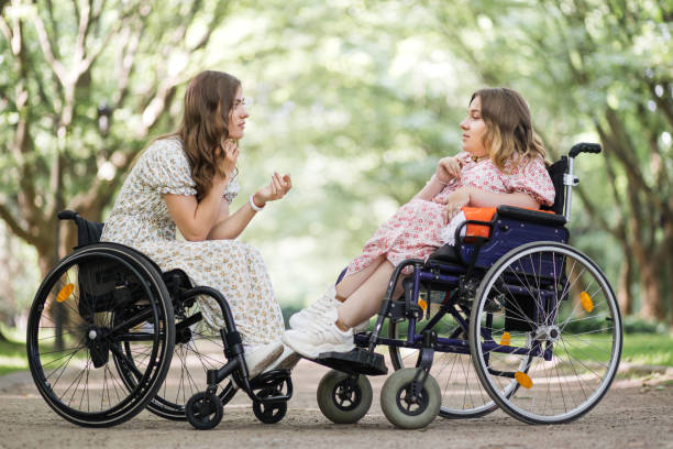 istock Two women in wheelchairs talking and smiling at park 1360508124