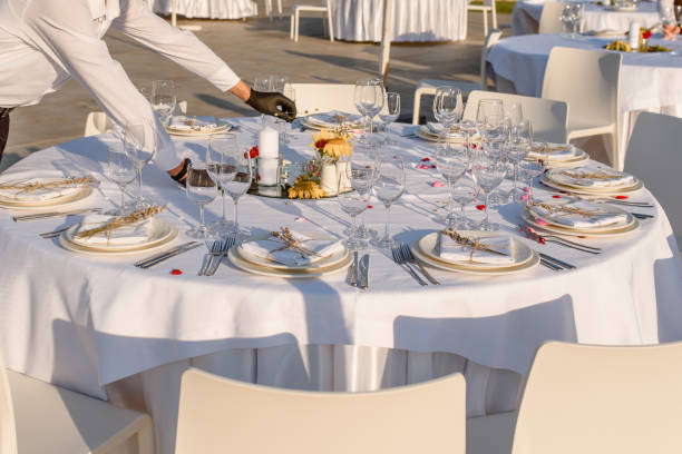 istock waiters hands in protective black gloves arrange a wedding party reception table decorated with flowers: plates, forks, knives and wine glasses. 1360509599