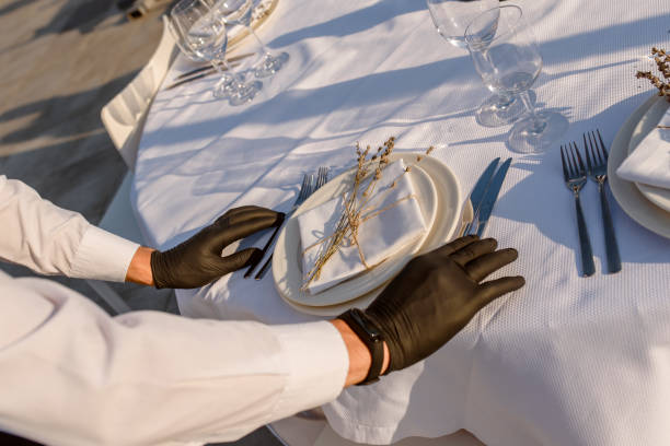 istock waiters hands in protective black gloves arrange a wedding party reception table decorated with flowers: plates, forks, knives and wine glasses. 1360509639
