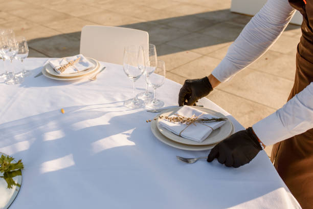 istock waiters hands in protective black gloves arrange a wedding party reception table decorated with flowers: plates, forks, knives and wine glasses. 1360509710