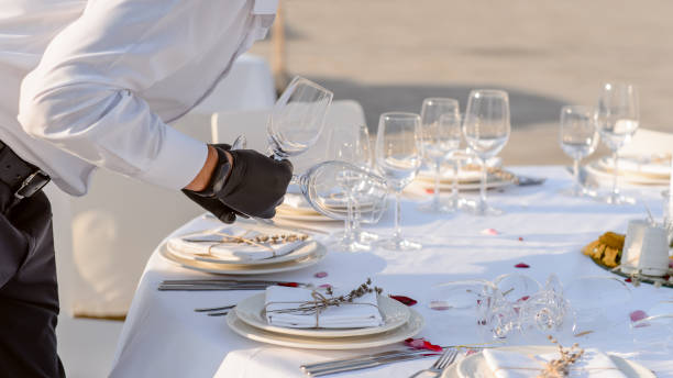istock waiters hands in protective black gloves arrange a wedding party reception table decorated with flowers: plates, forks, knives and wine glasses. 1360509770