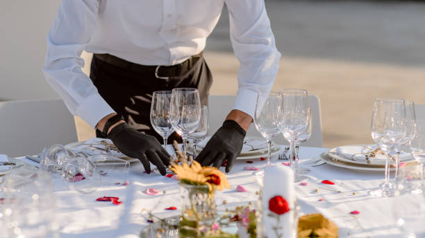 istock waiters hands in protective black gloves arrange a wedding party reception table decorated with flowers: plates, forks, knives and wine glasses. 1360509816