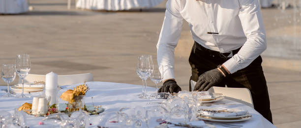 istock waiters hands in protective black gloves arrange a wedding party reception table decorated with flowers: plates, forks, knives and wine glasses. 1360510367