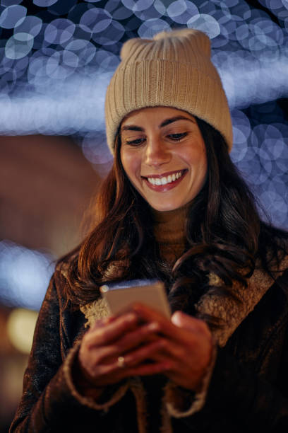 istock Smiling woman using phone outdoors in decorated city 1360510418