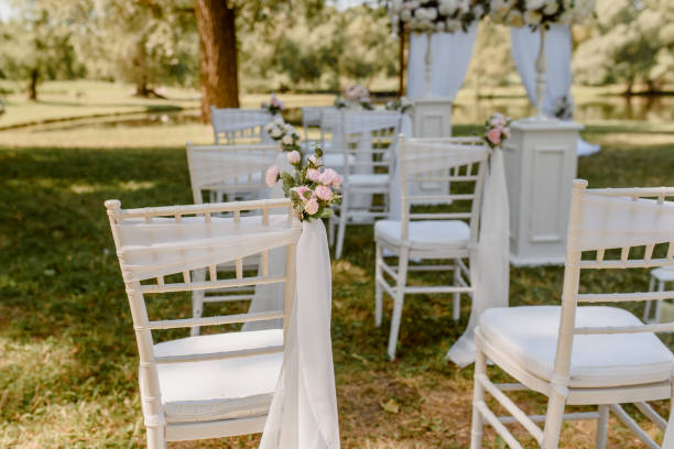 istock Wedding ceremony outdoors in the park. White chairs decorated with roses. 1360510773