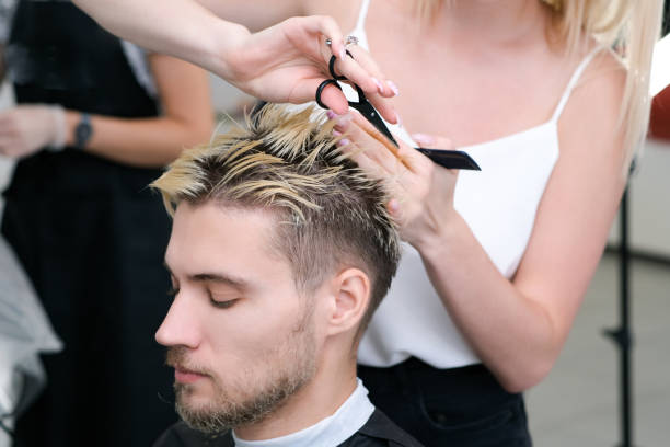 il parrucchiere taglia i capelli di un giovane con i capelli tinti biondi con le forbici in un salone di bellezza. - tagliare i capelli foto e immagini stock