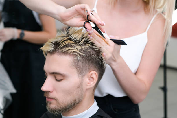 hairdresser cuts the hair of a young man with blond dyed hair with scissors in a beauty salon. - saç kesmek stok fotoğraflar ve resimler