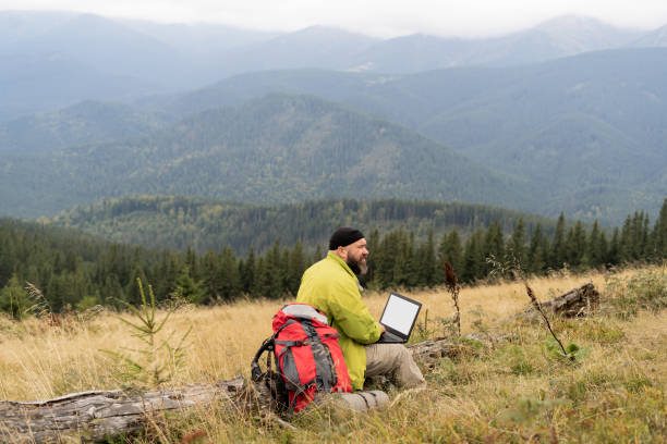 istock a bearded Caucasian man with a laptop sits on a fallen tree in the mountains with a beautiful view of the valley. 1360514535