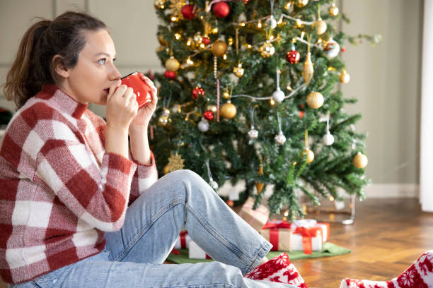istock Young woman drinking coffee by the Christmas tree 1360516844