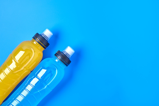 Close up isotonic energy orange yellow and blue sport drink in plastic bottles on blue background. Allows to maintain the most optimal balance of water, salt and electrolytes when playing sports