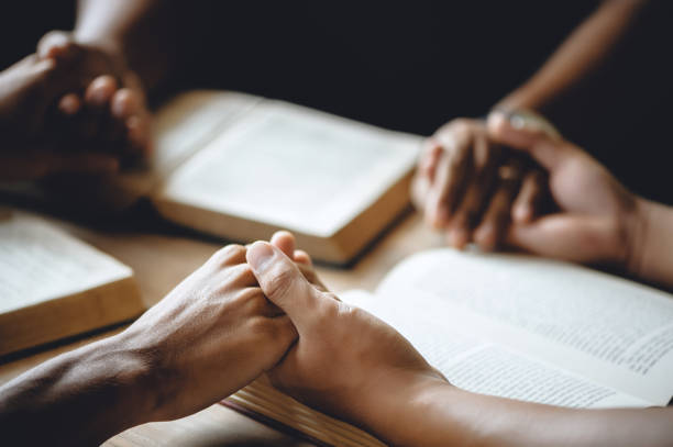 Christian group of people holding hands praying worship to believe and Bible on a wooden table for devotional or prayer meeting concept. stock photo