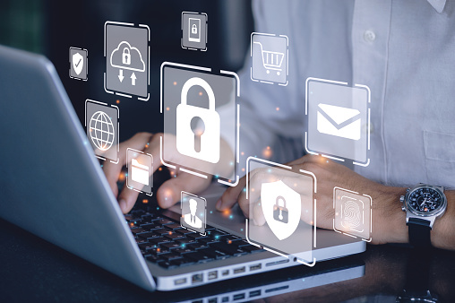 A close-up of hands typing on a laptop keyboard with digital icons of locks, shopping carts, and other security-related symbols floating above, suggesting a theme of online security and privacy.