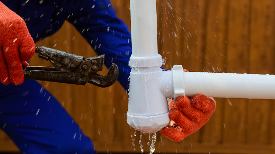 Plumbing repair concept. Hands in protective gloves are holding a wrench and fixing the leaking pipe