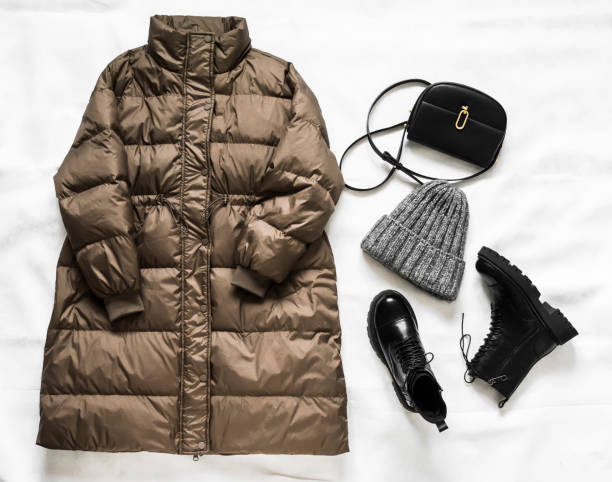 istock A set of women's winter clothes -a warm comfortable down jacket, leather boots with fur, a hat and a leather bag on a light background. top view. Fashion season concept 1360523095