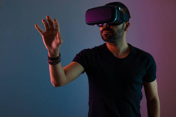 istock Young man in VR glasses headset interact with virtual reality in color neon light, future technology, education video gaming 1360531503