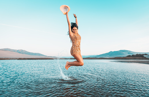 young latin woman jumping in the water outdoors smiling happy  with dental braces