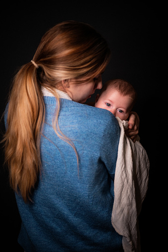 Close-up of a young woman holding a baby boy in her arms. Studio shot on a dark background