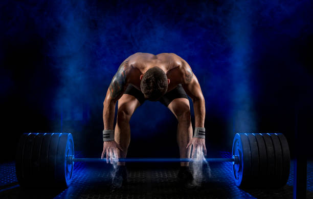 Sporty muscular man working out with barbell at a gym