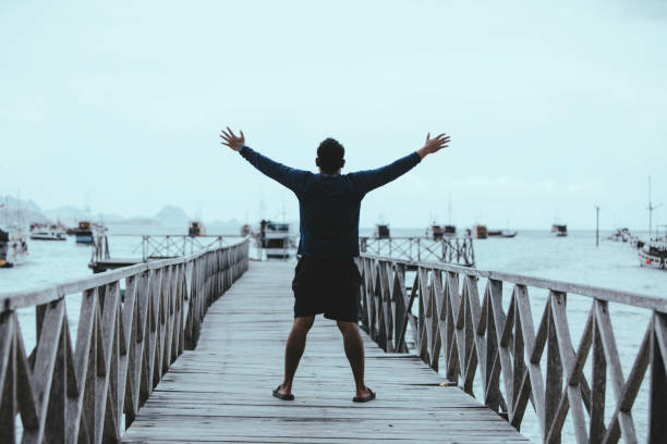 istock Young asian man arm raised when standing  on bridge 1360538764