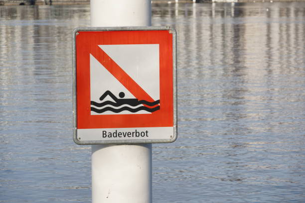 Square shaped signpost saying in German bathing prohibited attached on a metal pole. Placed in Lake Lucerne in Switzerland. The lake itself is on the background. It is warning symbol against danger.