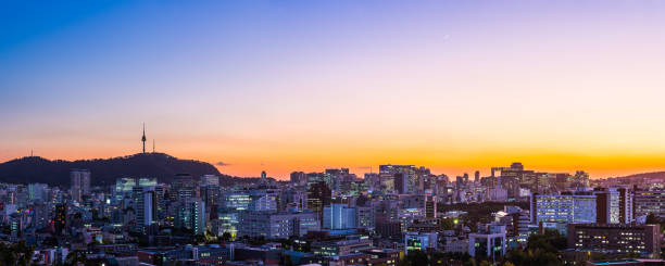 The iconic spire of Namsan Tower on the mountain at sunset overlooking the warmly illuminated highrise cityscape of central Seoul, South Korea’s vibrant capital city.