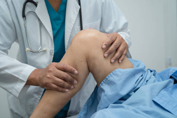Asian doctor physiotherapist examining, massaging and treatment knee and leg of senior patient in orthopedist medical clinic nurse hospital. stock photo