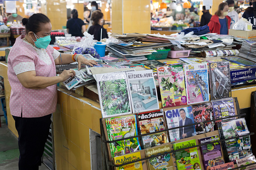 Chiang Mai, Thailand - December 14, 2021 : Unidentified woman sorting newspapers on stall in fresh market at Chiang Mai, Thailand.