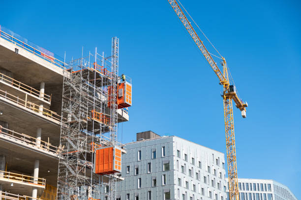 istock Construction site with lift on scaffolding and crane against blue sky 1360551656