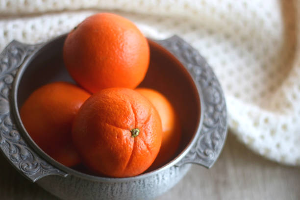 Bowl of Oranges and Blanket Silver bowl filled with fresh oranges and soft knitted blanket on wooden background. Selective focus. antique fruit bowl stock pictures, royalty-free photos & images