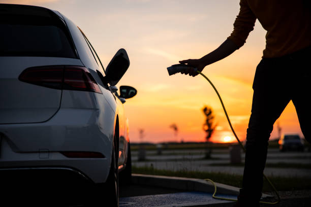 silhouette des mannes, der den stecker in die ladebuchse des elektroautos steckt - hineinstecken stock-fotos und bilder