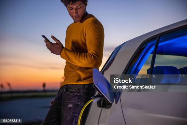 Man Using Mobile Phone While Charging Electric Car Stock Photo - Download Image Now - Electric Car, Car, Charging