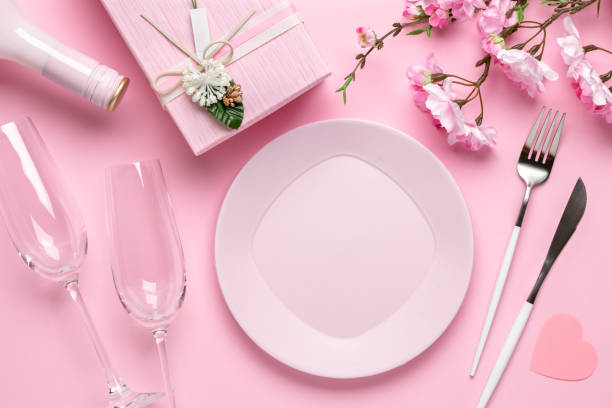 Romantic dinner, table setting on Valentine's Day. Dating concept, love. Spring flowers, empty plate, glasses, champagne, gift box, cutlery on a festive pink background. stock photo