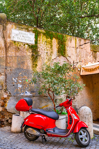 Rome, Italy, December 16 -- A characteristic Vespa scooter parked in Vicolo di Santa Maria in Trastevere, an ancient alley of the Rione Trastevere, in the historic heart of Rome. A detail on the sign with the name of the street indicates R.XIII at the top right, which marks in Roman numerals the XIII district of Trastevere of the 22 historic districts of Rome. Trastevere is an iconic quarter of the Eternal City, due to the presence of countless artistic and historical treasures, monuments and ancient Romanesque and Baroque churches, but also for its squares and hidden alleys to be explored freely, where it is easy to find typical restaurants, pubs, small shops of artisans and scenes of daily life with the original Roman soul. In 1980 the historic center of Rome was declared a World Heritage Site by Unesco. Image in high definition format.