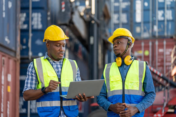 istock African workers, Engineer, Technician holding laptop for checking and inspecting on site containers area for shipping transportation and machine lifting. Concept people operation in heavy industrial. 1360557157