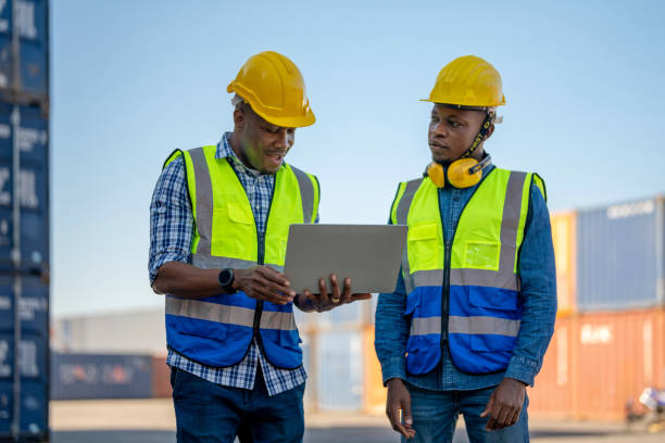 istock African workers, Engineer, Technician holding laptop for checking and inspecting on site containers area for shipping transportation. Concept people operation in heavy industrial. 1360557294