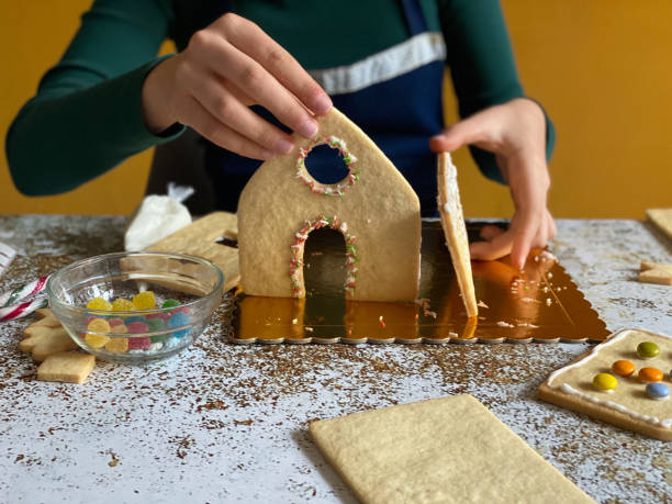 istock girl hands assembling gingerbread house at home 1360558074