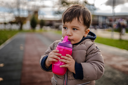 Baby Boy está bebiendo un recipiente para biberones de agua mientras está en el parque photo
